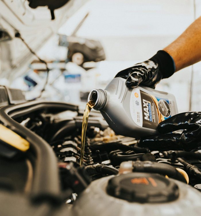 Close-up of a mechanic pouring engine oil into a car engine in an auto repair shop.